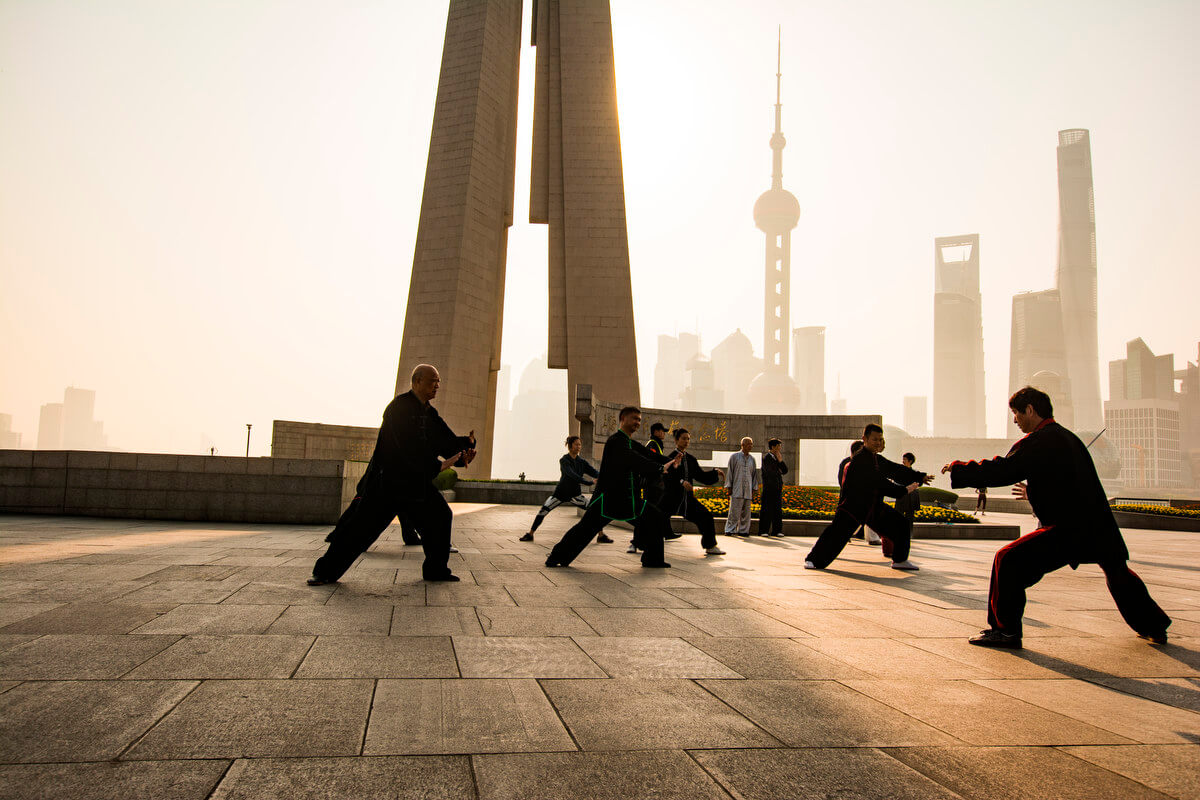 Chinese people dressed in black doing morning tai chi against a backdrop of modern skyscrapers.